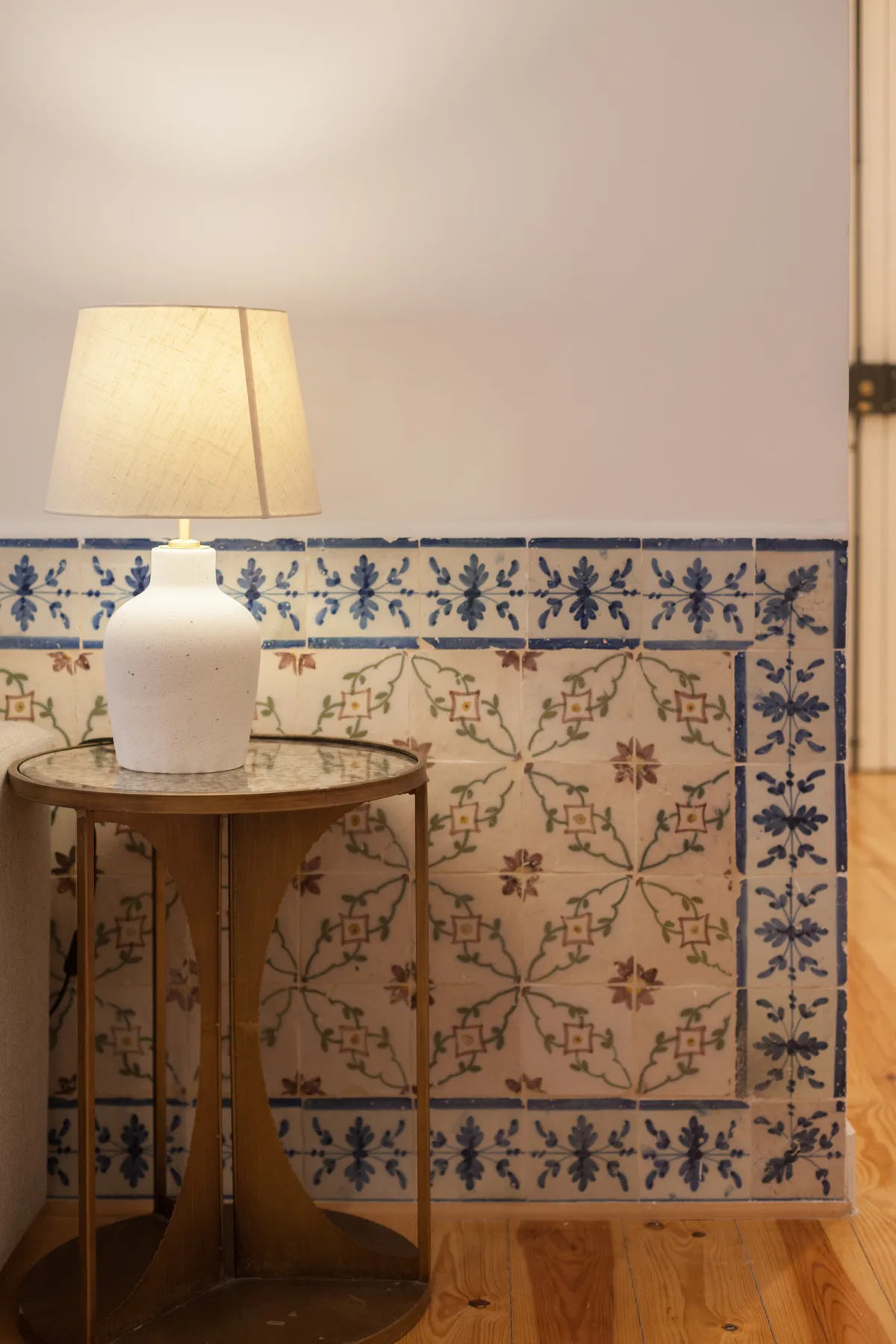 Una pared interior de azulejos junto a una mesa pequeña con una lámpara encendida.