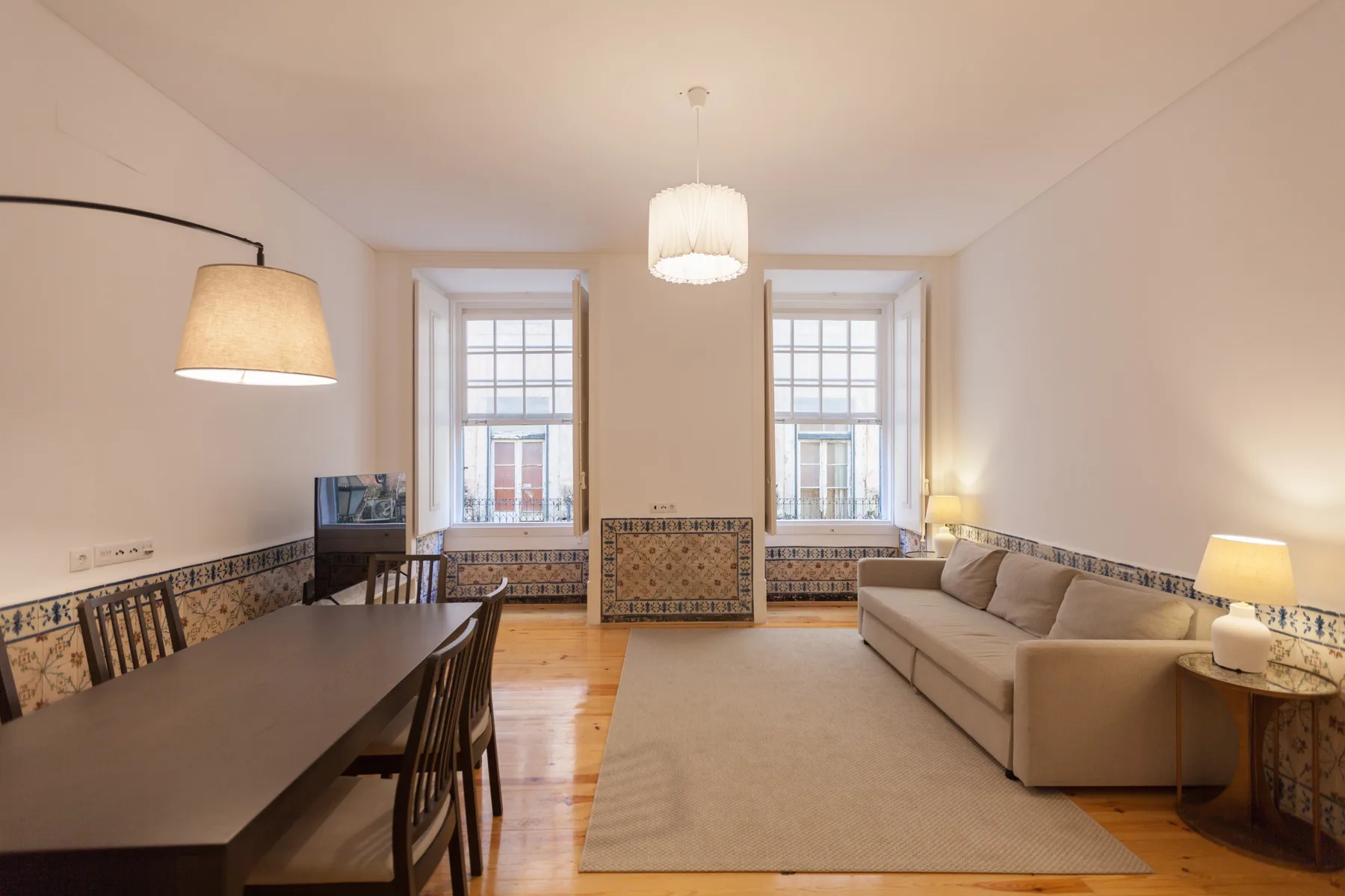 Una sala de estar con mesa de comedor, asientos y dos ventanas.
