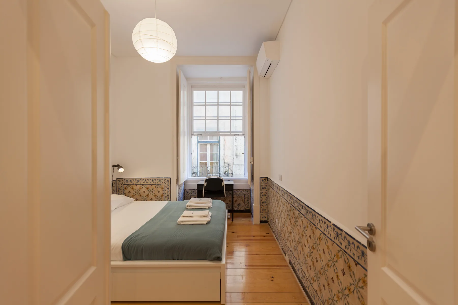 Un dormitorio con una cama, azulejos decorados en la pared y una ventana alta.