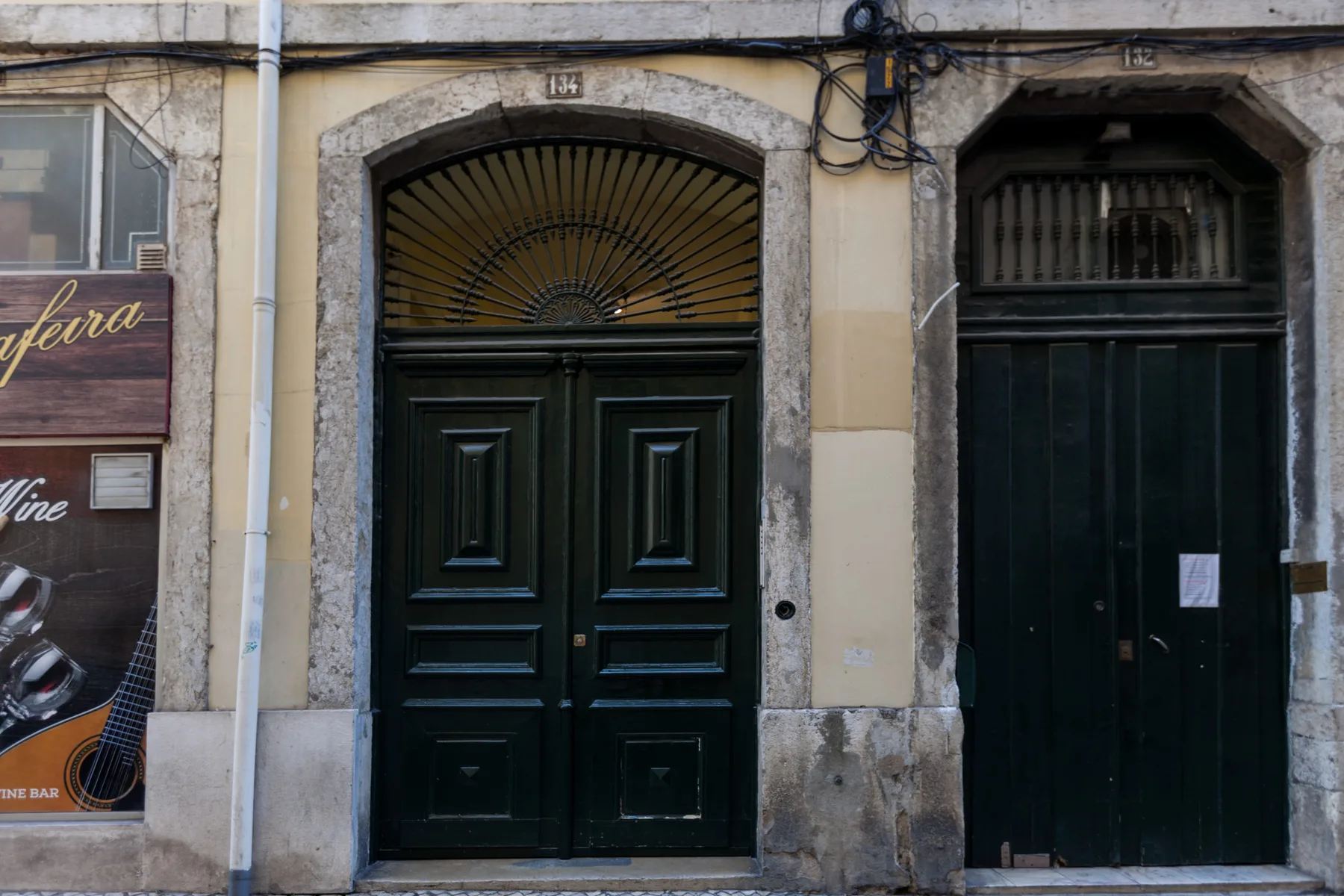 Entrada de edificio a la calle con una puerta oscura panelada y un montante en arco.
