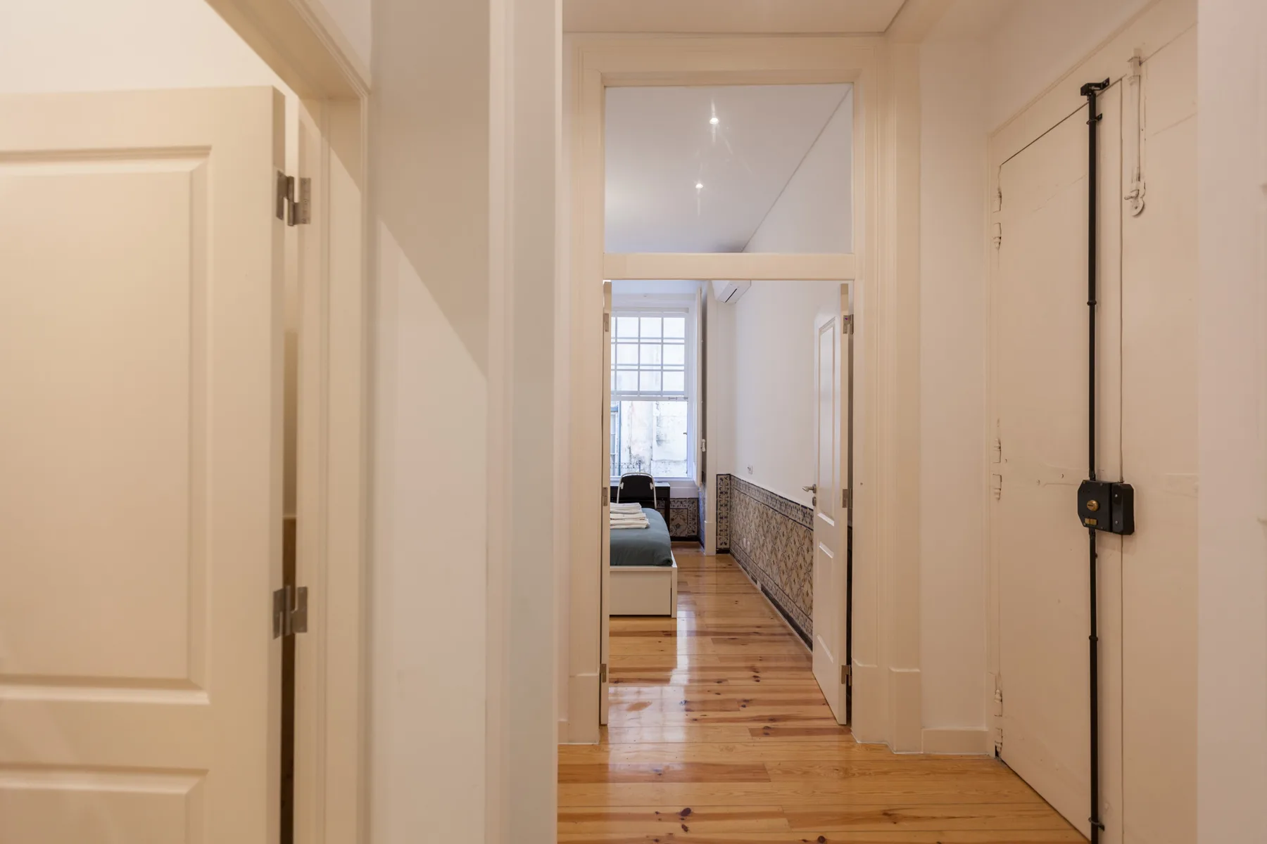 Un pasillo estrecho con suelo de madera conduce a una habitación luminosa.