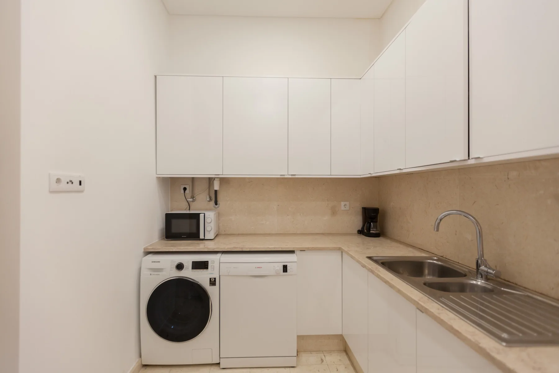 Una cocina compacta con armarios blancos, una lavadora y un fregadero doble.