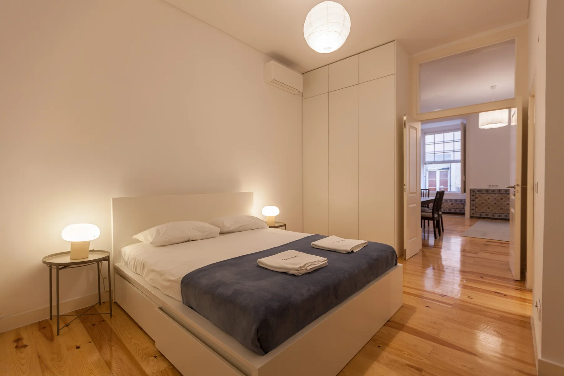 Dormitorio con una cama, mesas de noche y una puerta hacia otra habitación.