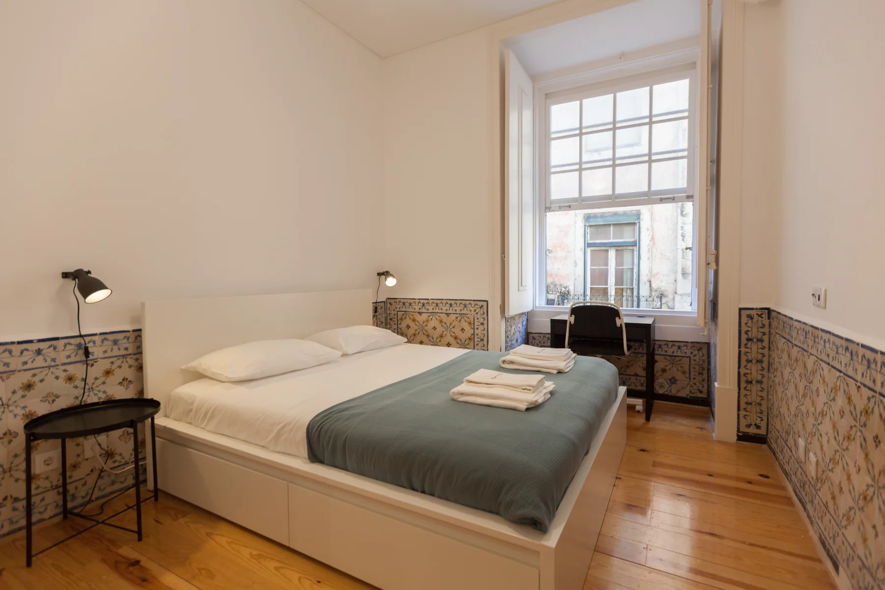 Un dormitorio con una cama, detalles de azulejos estampados y una ventana con vistas a la calle.