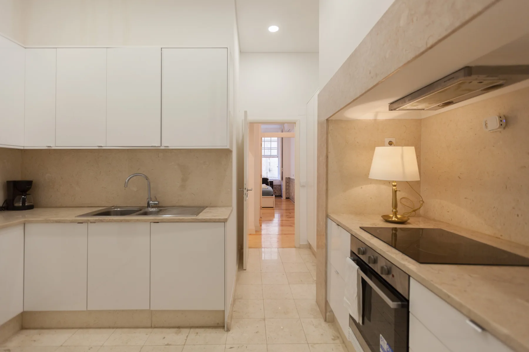 Una cocina luminosa con armarios blancos, encimeras y un pasillo central.