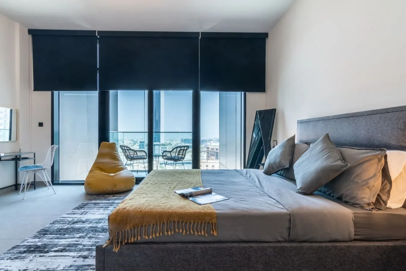 Un dormitorio con una cama grande junto a ventanales y persianas oscuras.