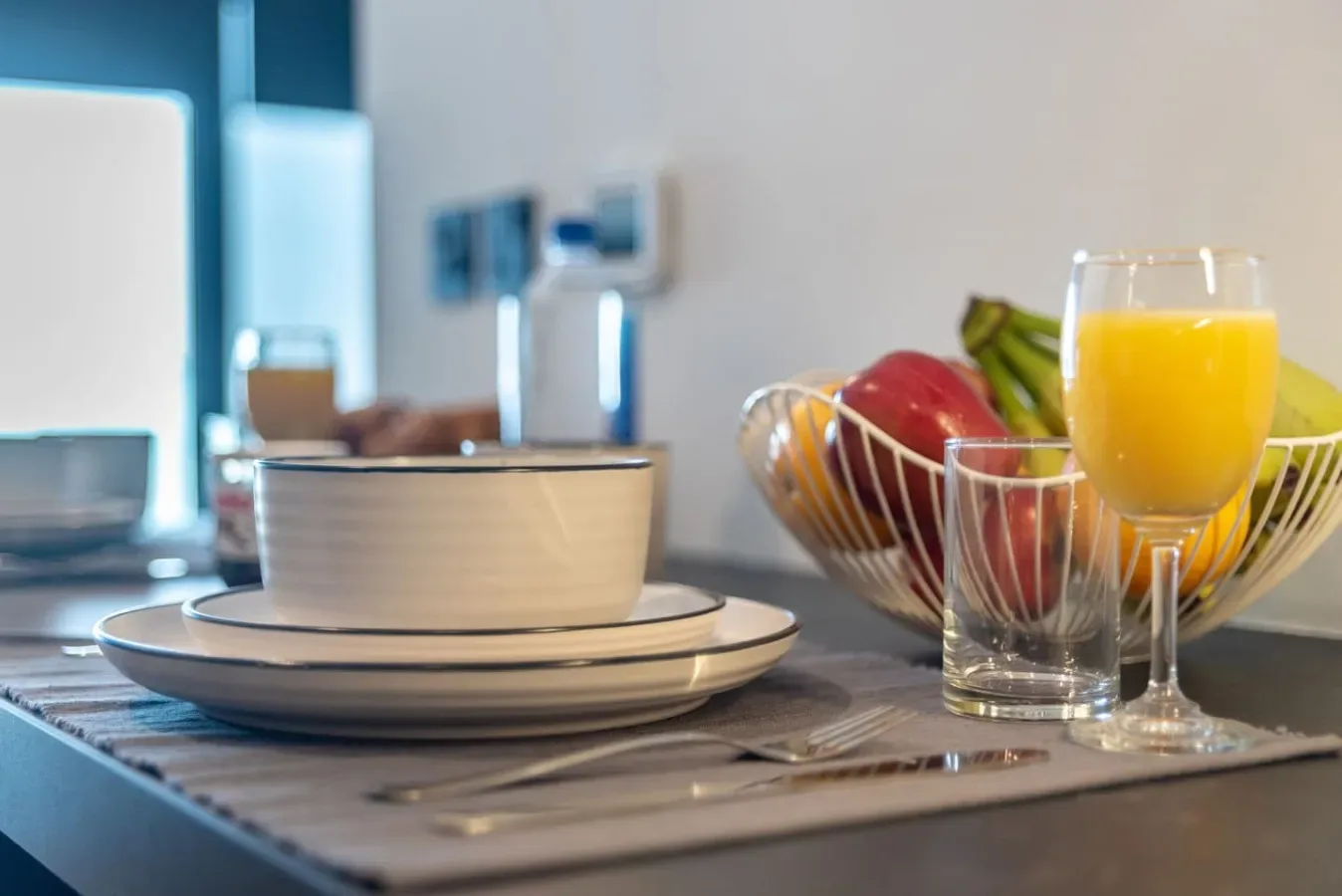 Una mesa está preparada con platos, un cuenco, fruta y vasos de zumo.