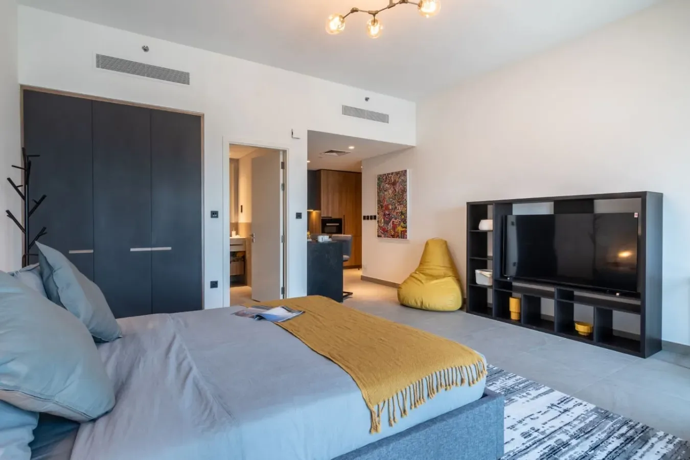 Un dormitorio con una cama, un televisor y un sillón puff amarillo.