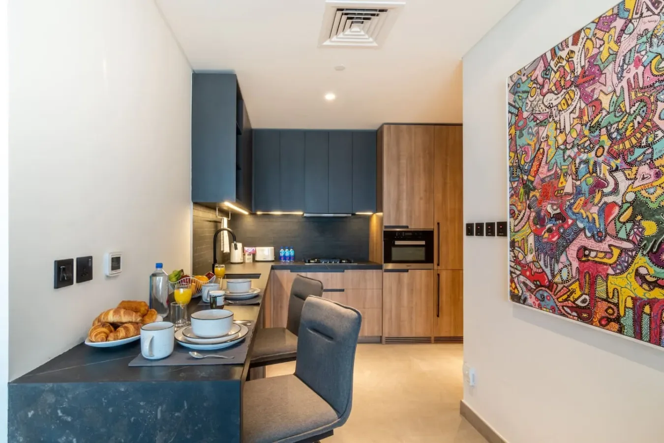 Una cocina compacta con gabinetes oscuros, una encimera y arte colorido en la pared.