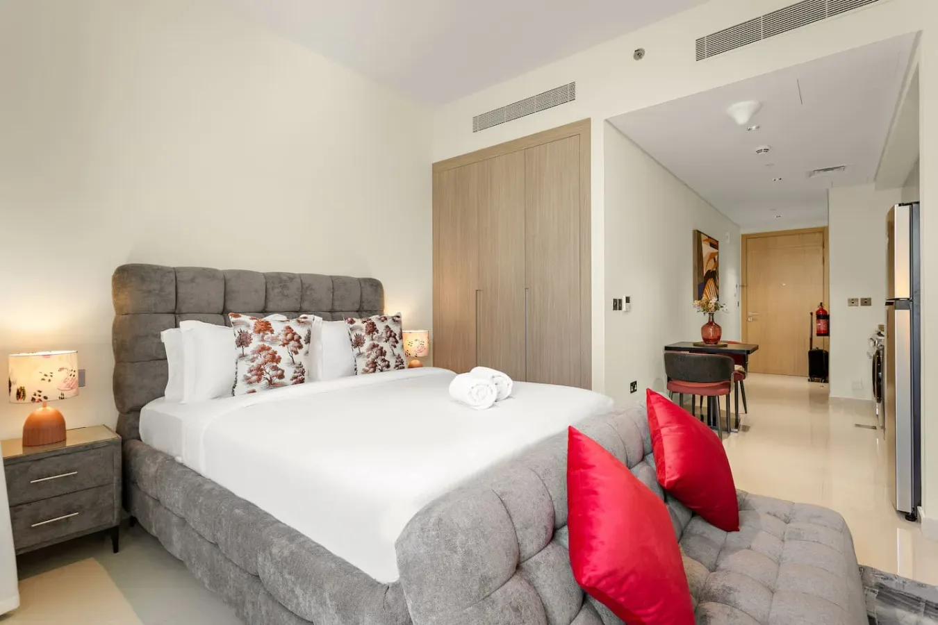 Un dormitorio con una cama bien hecha y una pequeña zona de comedor al fondo.