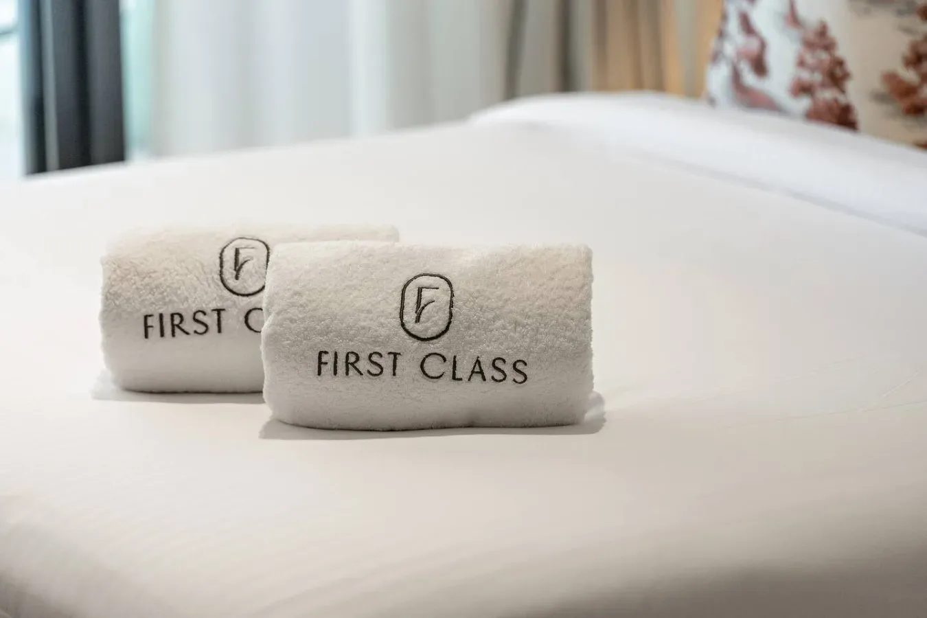 Una cama bien tendida con toallas dobladas bordadas con «First Class».