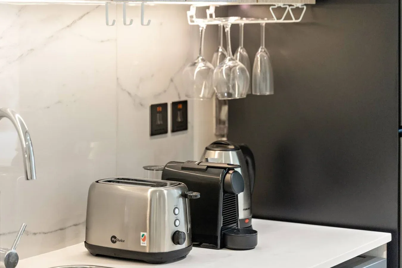 Una encimera de cocina con una tostadora y una cafetera bajo copas colgantes.