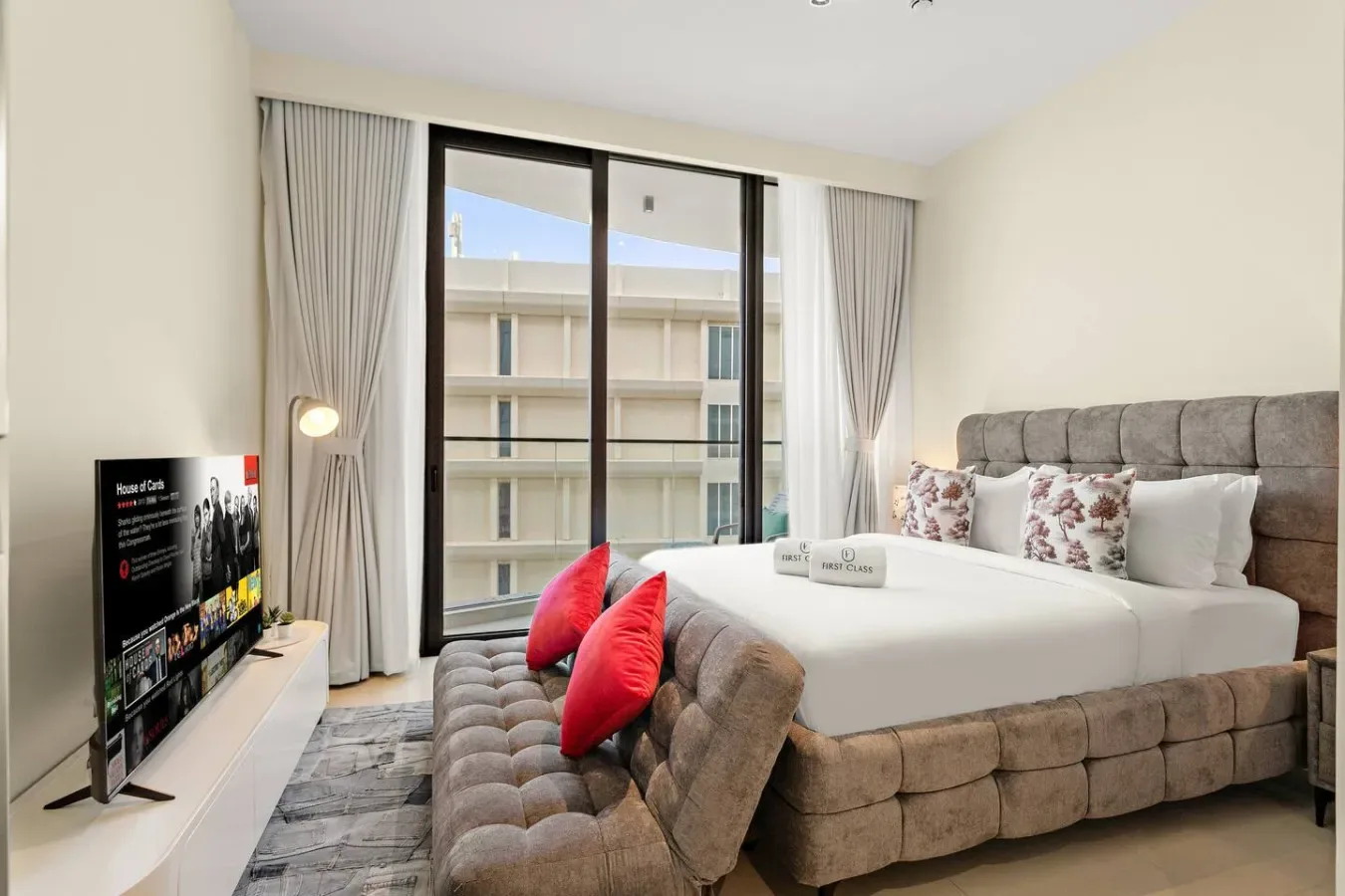 Un dormitorio luminoso con una cama grande, ventanales y un asiento acolchado.