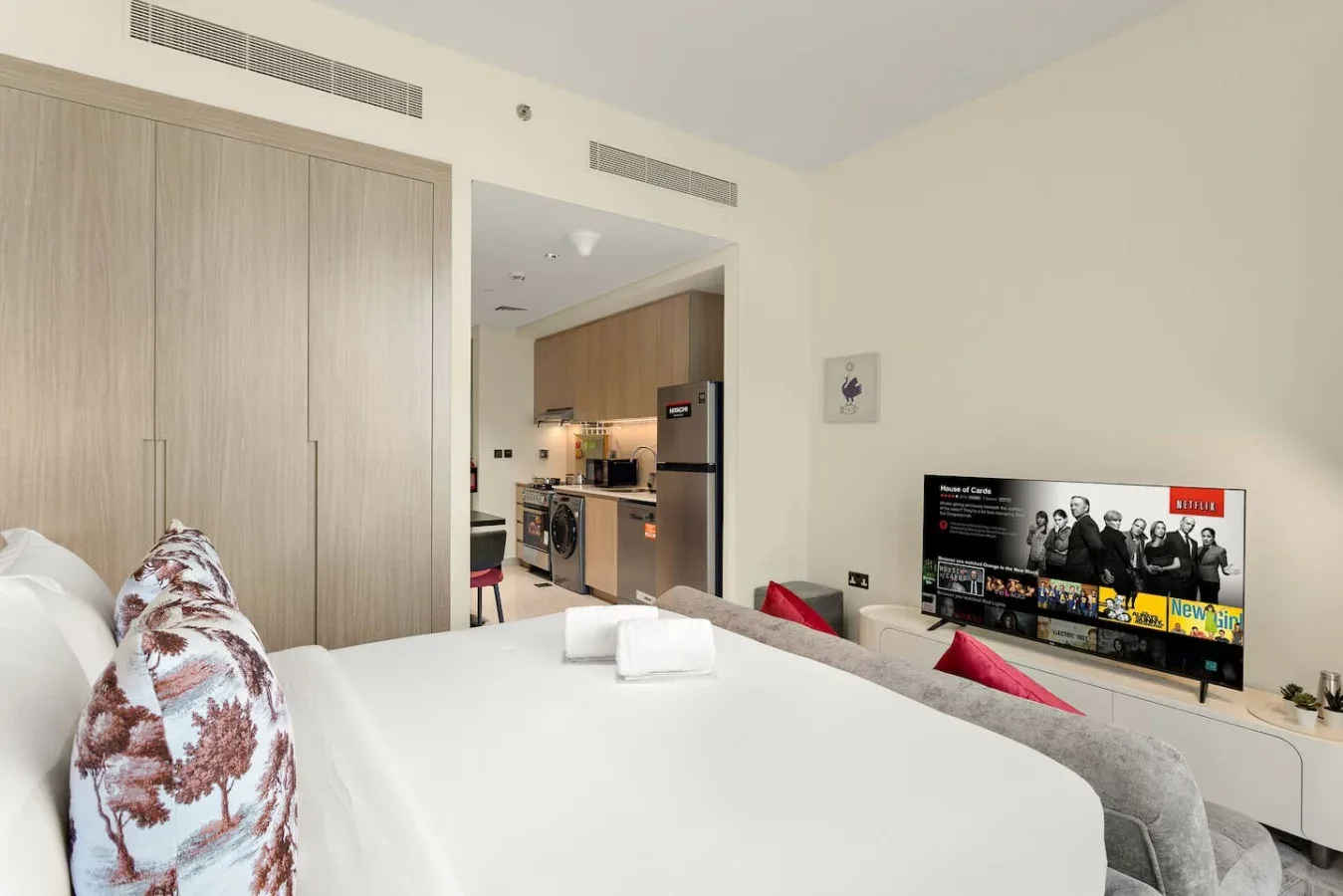 Dormitorio con una cama bien arreglada y una cocina abierta al fondo.