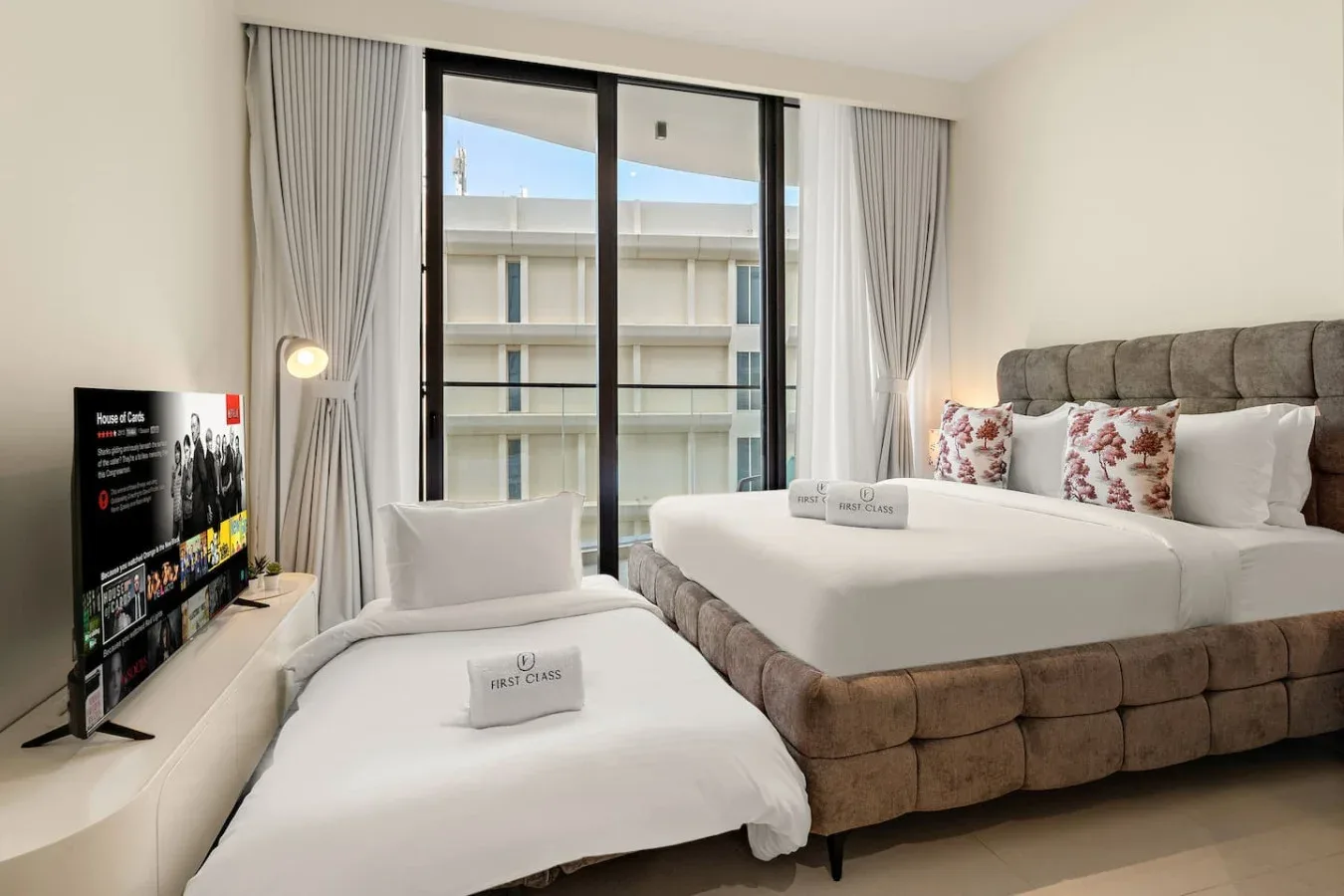 Un dormitorio con una cama grande, una cama individual y ventanas con vistas a un edificio cercano.