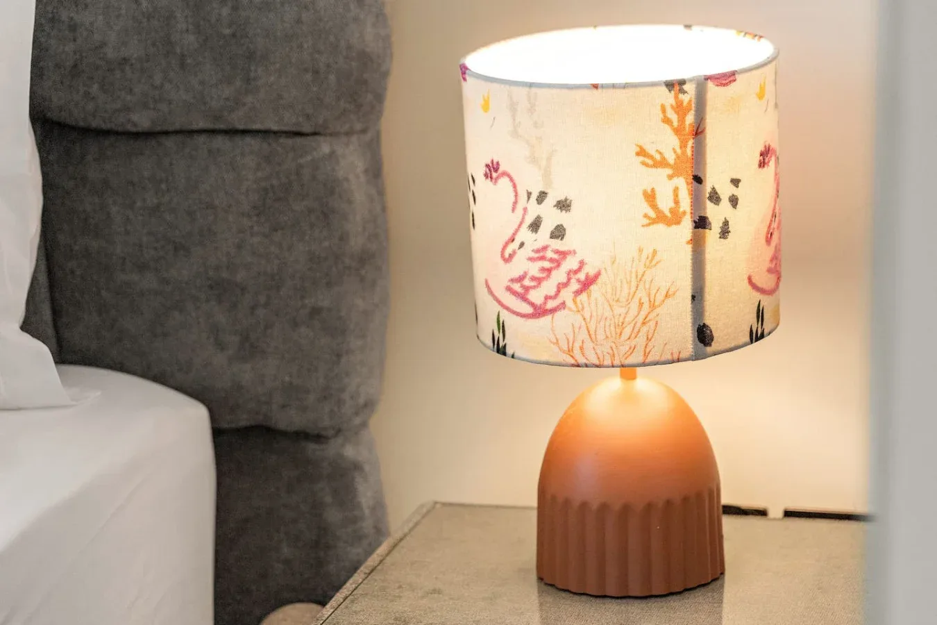 Una lámpara de mesa con pantalla estampada está junto a una cama.