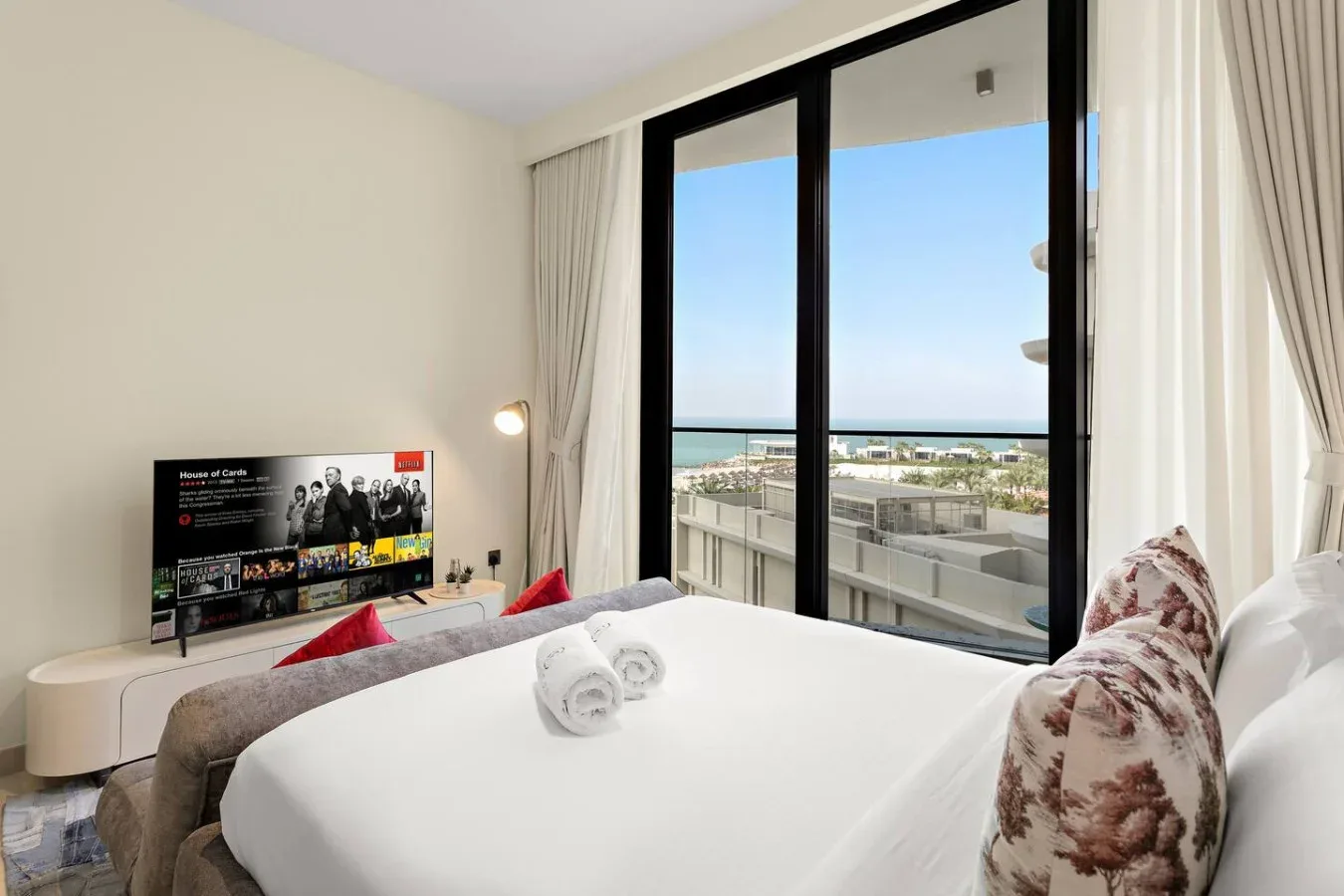 Un dormitorio luminoso con una cama bien hecha junto a una gran ventana con vistas al mar.