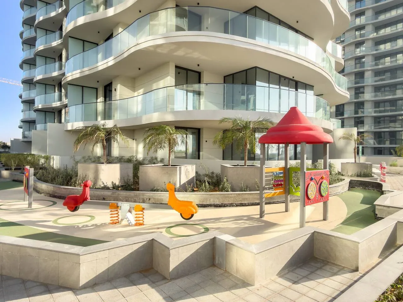 Un colorido parque infantil al aire libre está frente a un edificio de apartamentos moderno.