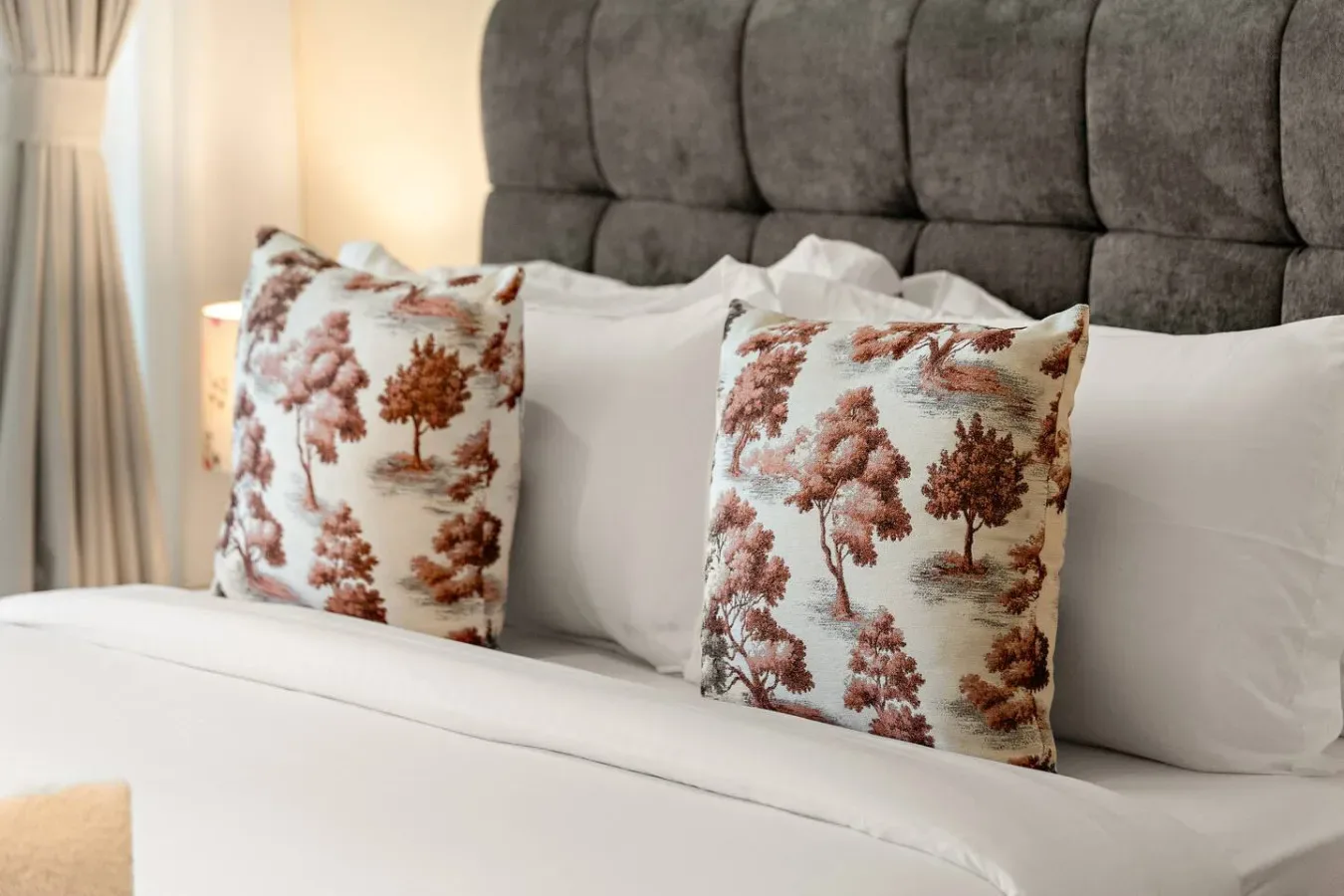 Una cama de dormitorio con ropa de cama blanca y cojines decorativos estampados.