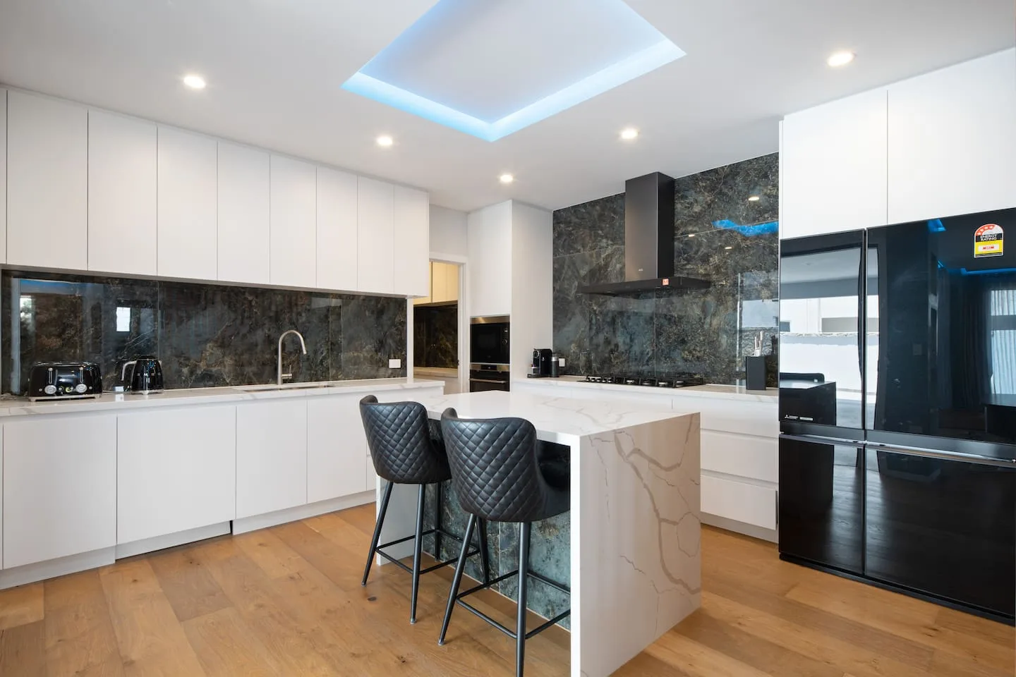 Una cocina moderna y luminosa cuenta con gabinetes blancos, encimeras oscuras y una isla con asientos.