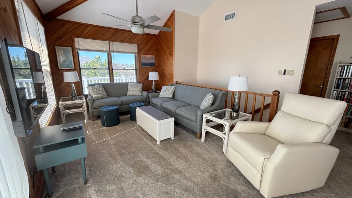 A bright living room with gray seating and a white armchair beside large windows.