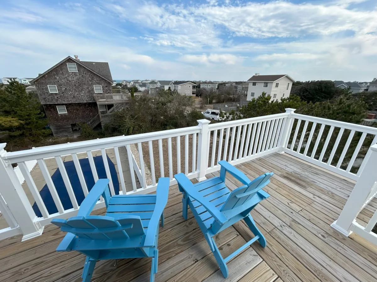 A wooden deck with blue seating overlooks nearby houses beneath a partly cloudy sky.