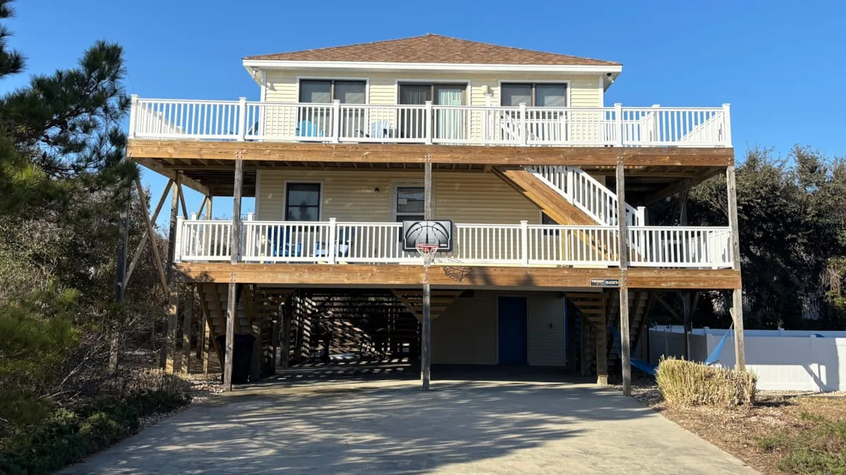 A raised two-story house has broad white-railed decks and a driveway.