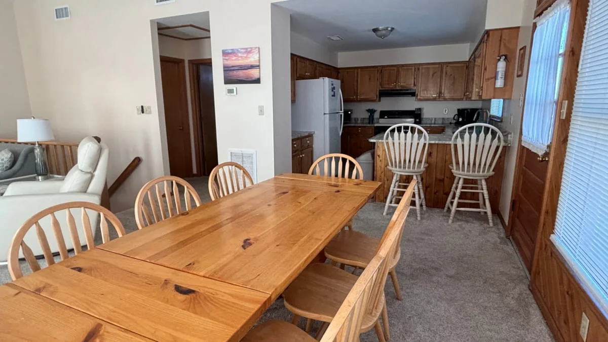 A dining area with a wooden table and chairs opens into a kitchen.