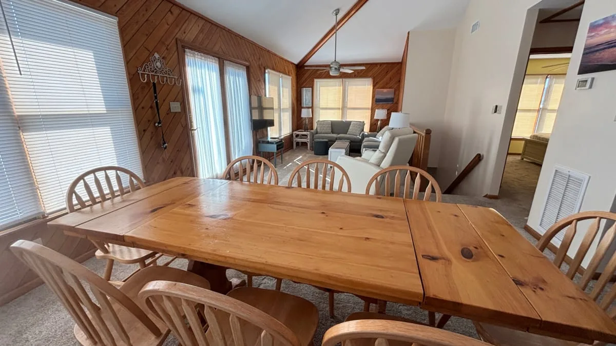 A dining area with a long wooden table and seating, opening into a living area.