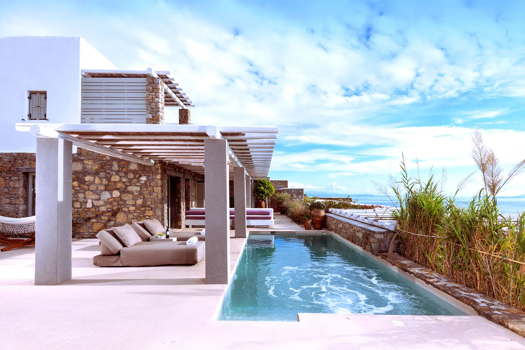 Una piscina junto a una zona de estar con sombra y muros de piedra.