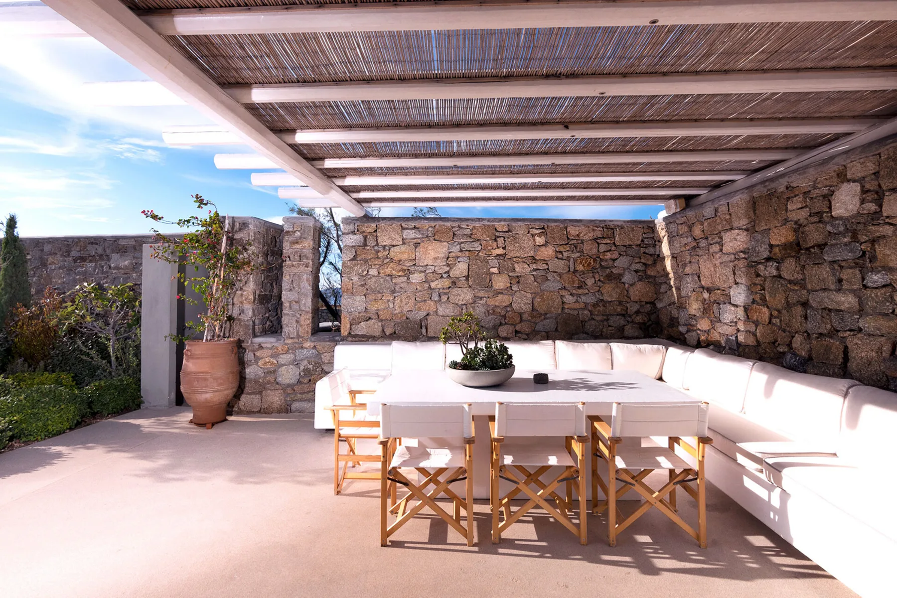 Una zona exterior cubierta tiene una mesa larga y bancos acolchados.