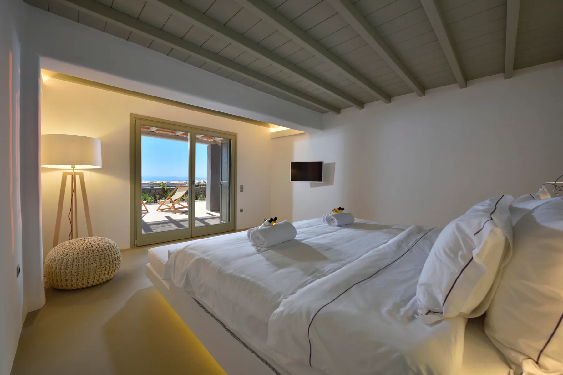 Un dormitorio luminoso con una cama grande, una lámpara de pie y puertas de cristal que dan a un balcón.