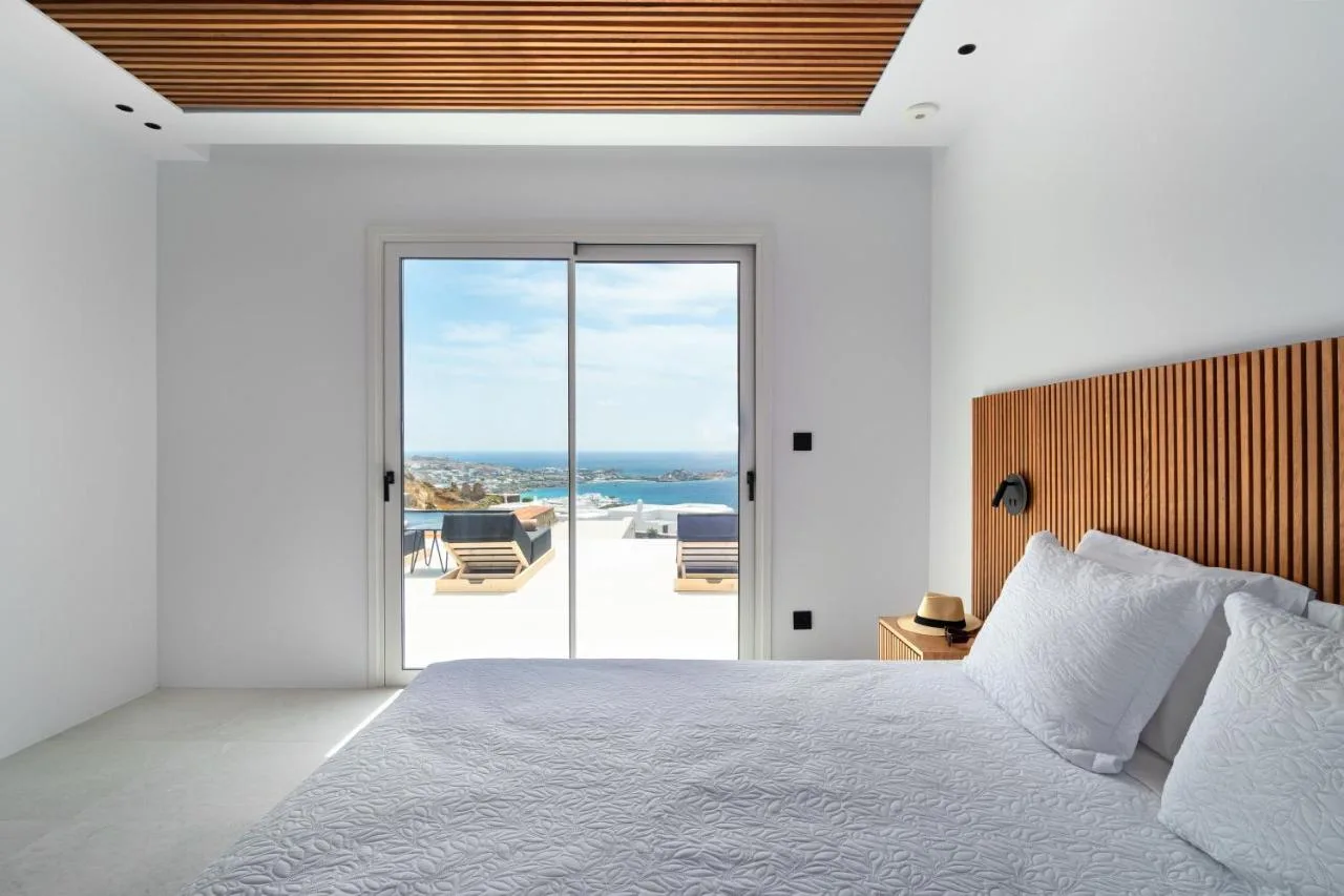 A bright bedroom with a large bed and sliding glass doors overlooking the sea.
