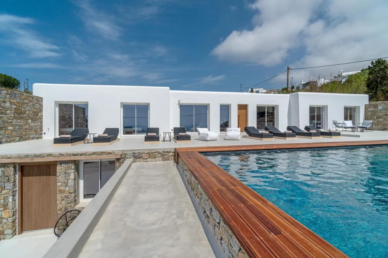 A modern white villa overlooks a swimming pool and outdoor seating area.