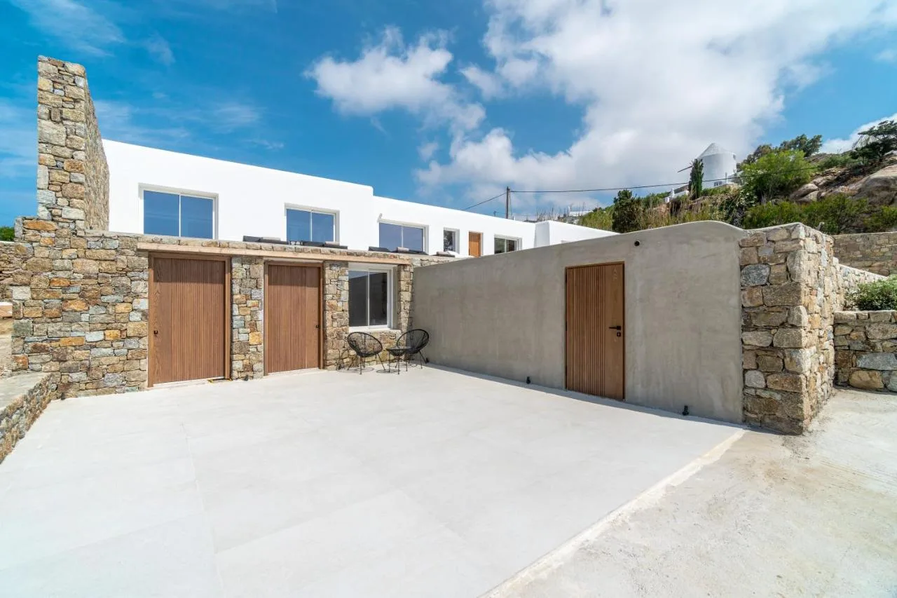 A modern villa exterior opens onto a broad paved courtyard with stone walls.