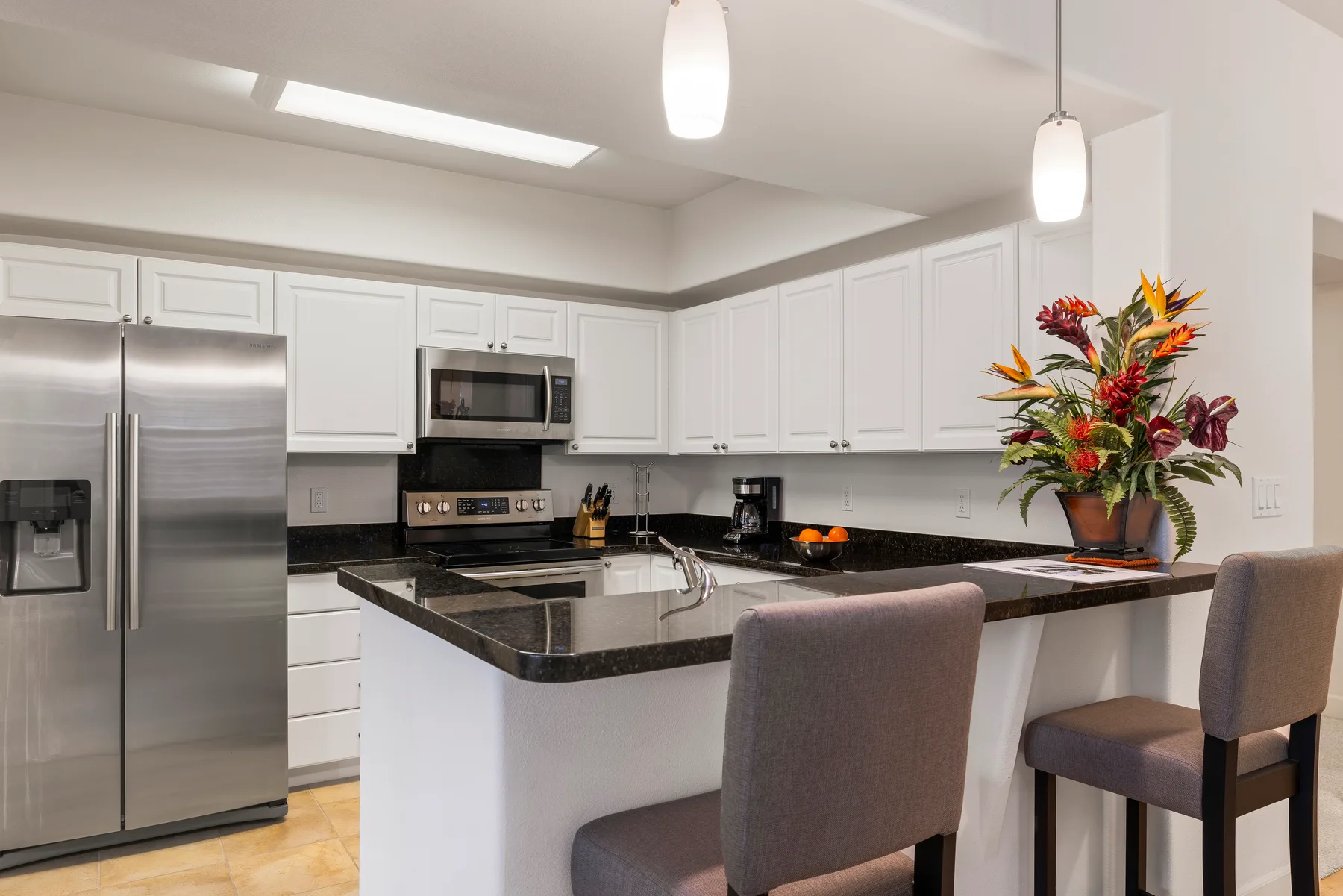 Una cocina luminosa con gabinetes blancos, electrodomésticos de acero inoxidable e isla central.