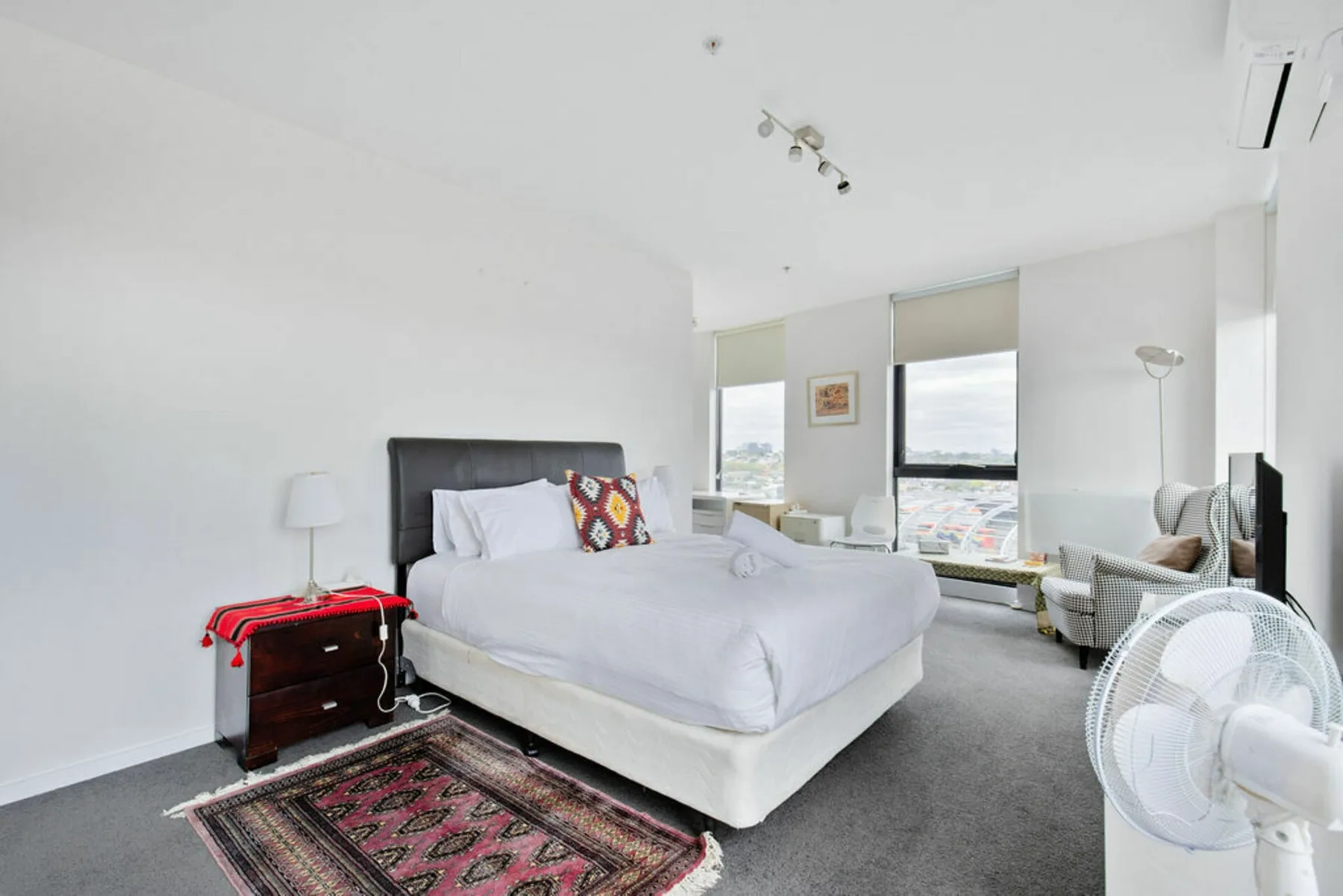 A bright bedroom with a bed, large windows, and seating.