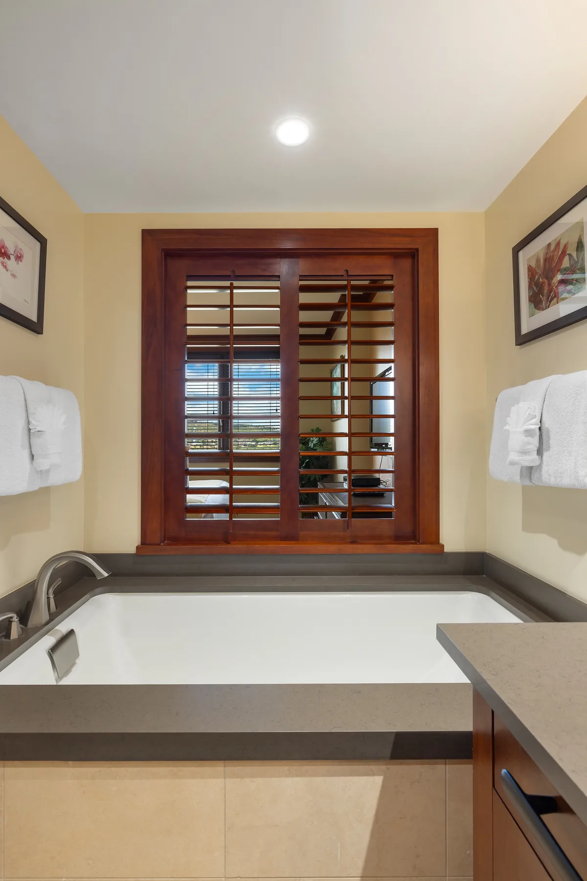 Un baño cuenta con una bañera grande bajo una ventana con marco de madera.