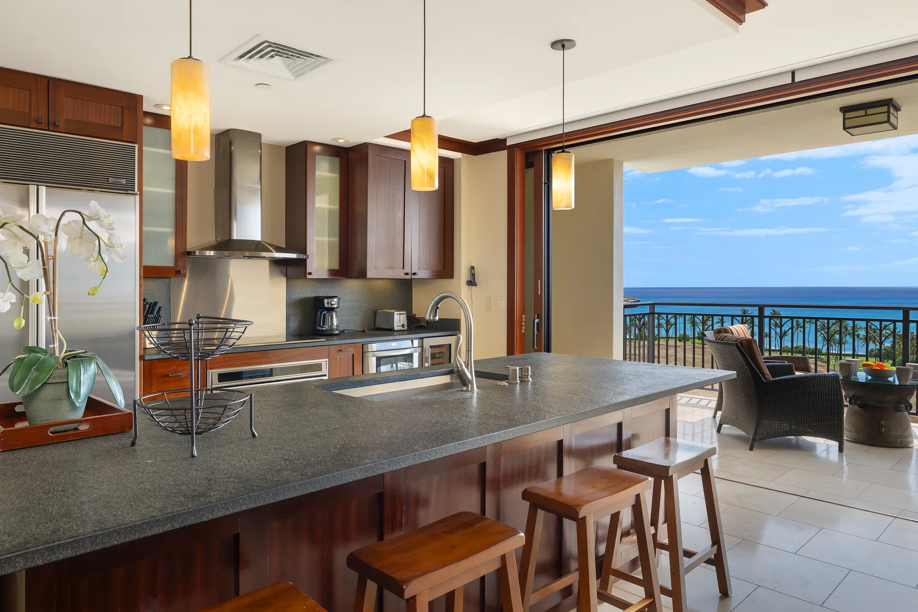Una cocina moderna con una amplia barra y taburetes se abre a un balcón con vistas al mar.