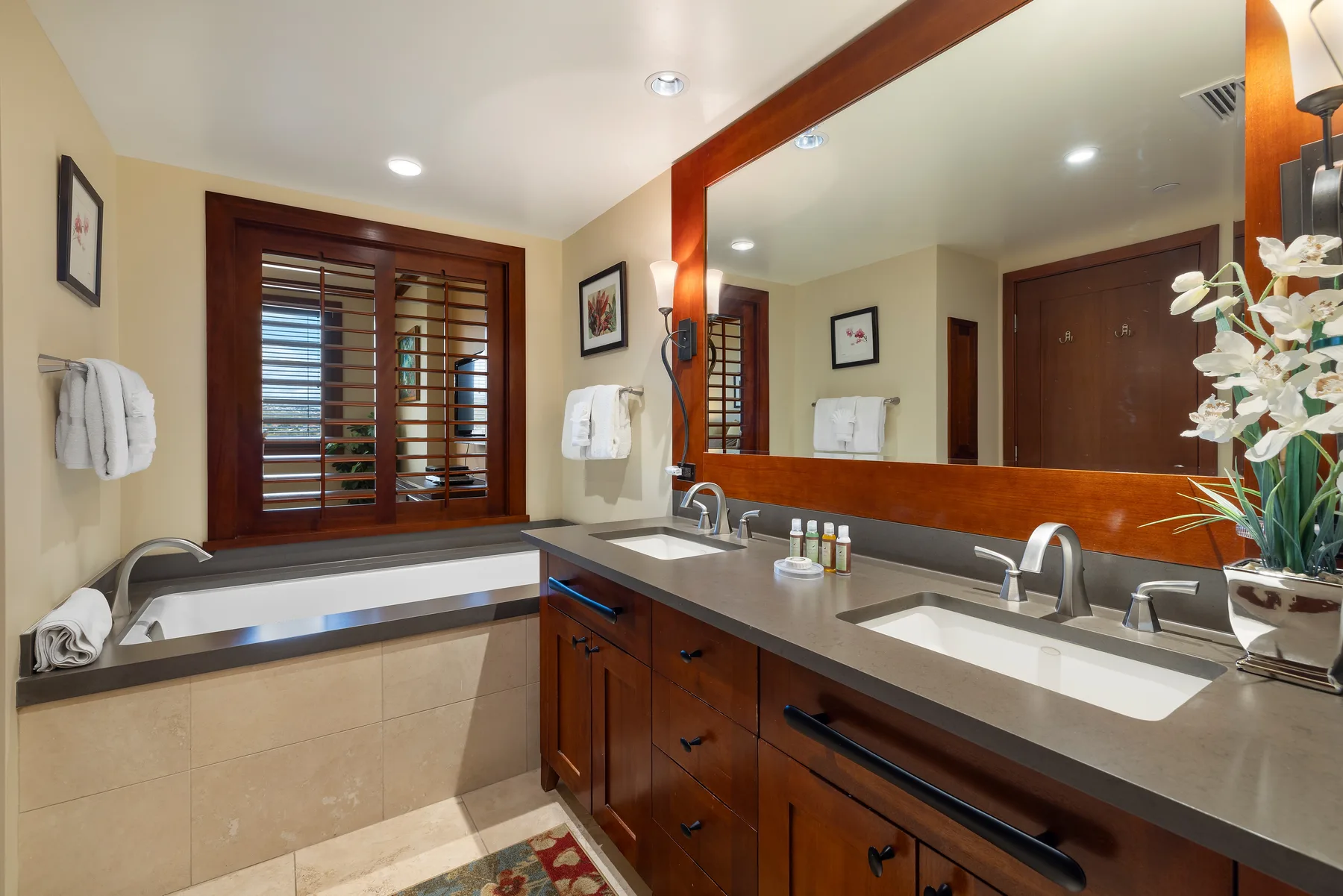 Un tocador de baño con un espejo grande, dos lavabos y una ventana con persianas de madera.