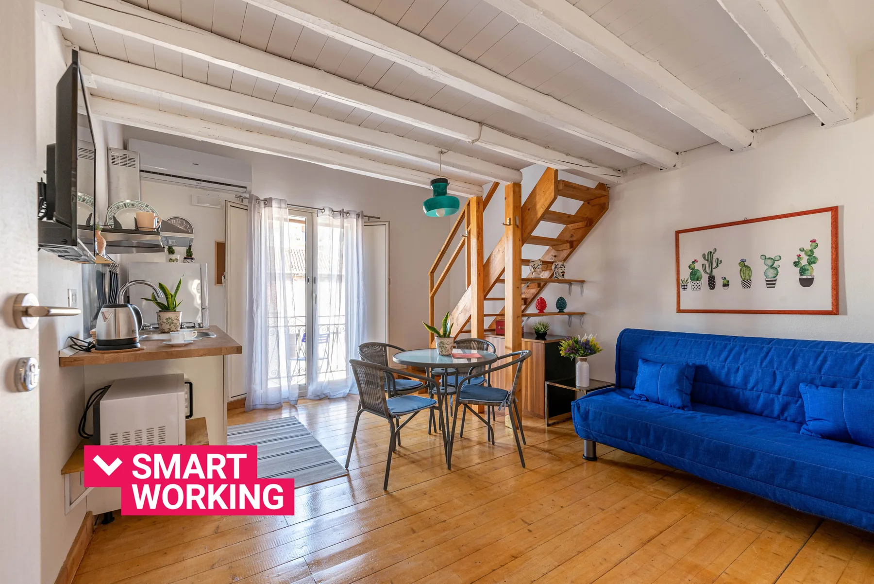 Una zona compacta de estar y comedor con un sofá azul y una escalera de madera.