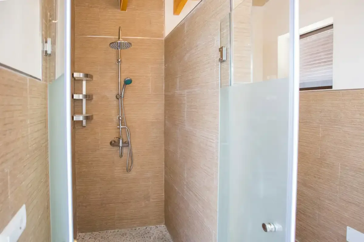 A tiled shower area with a wall-mounted showerhead and handheld shower.