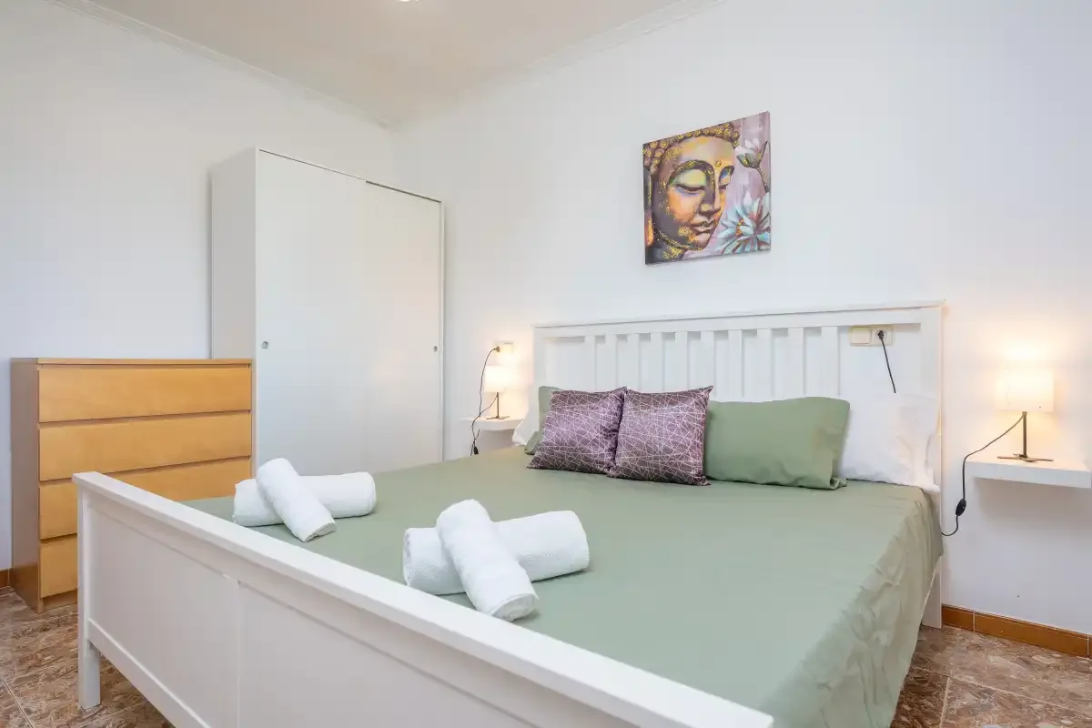 A bedroom with a bed, folded towels, and colorful artwork above the headboard.