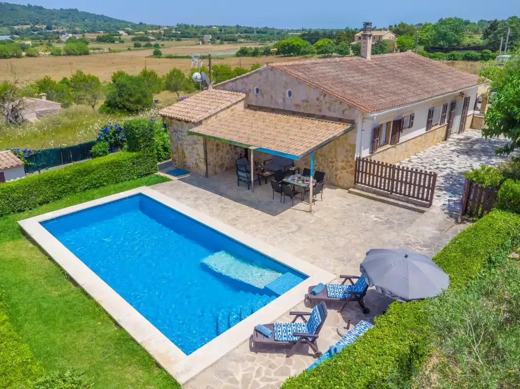 A countryside house beside a swimming pool, with outdoor seating and surrounding fields.