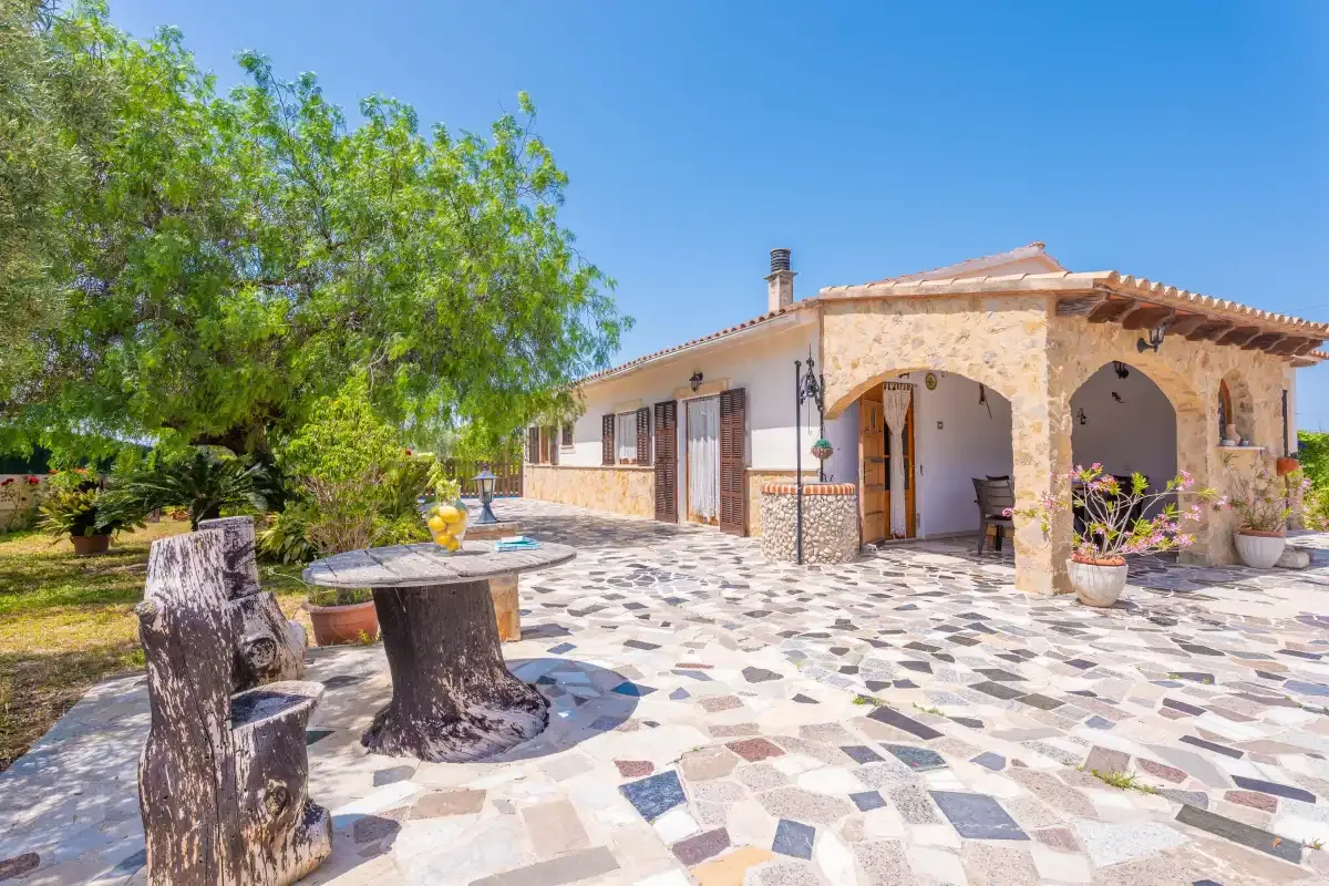 A stone-paved outdoor patio beside a house, with a shaded arched porch.