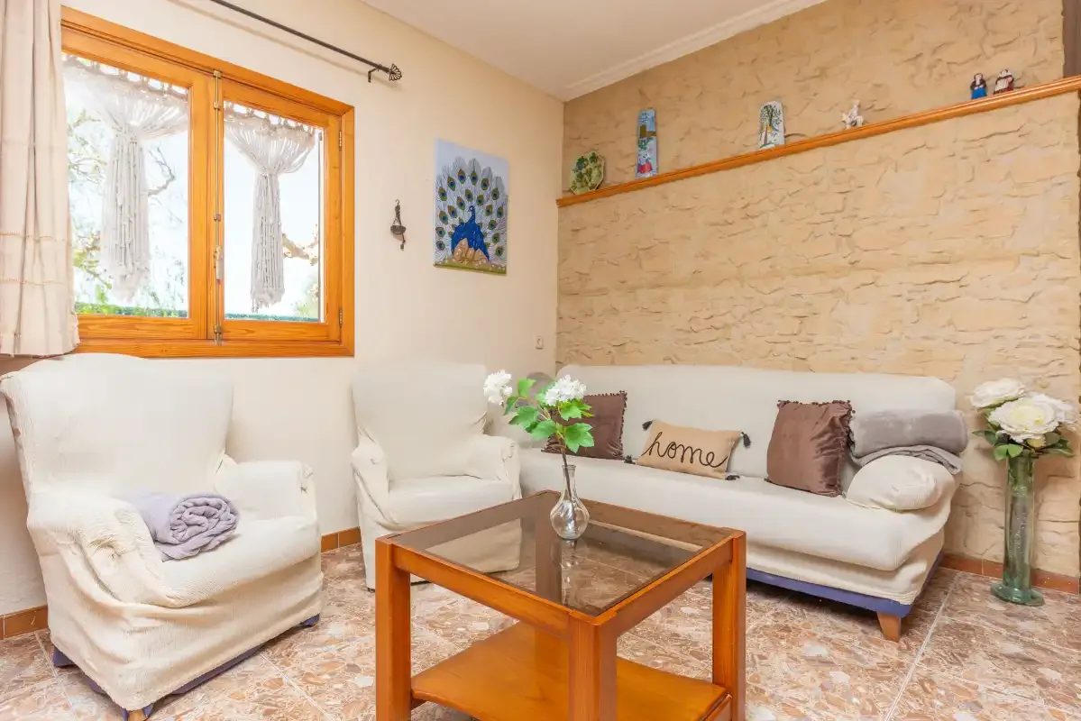 A living room with white seating, a wooden coffee table, and a stone-textured wall.