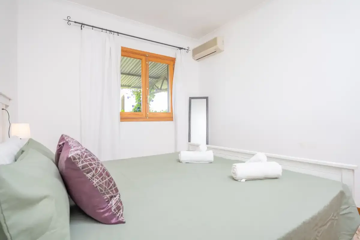 A bedroom with a large bed, a window, and a wall-mounted air conditioner.