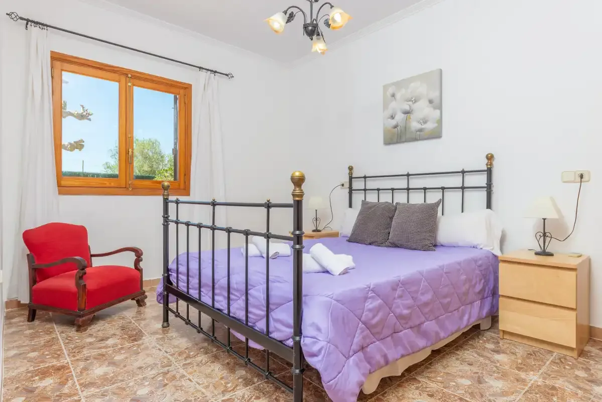 A bedroom with a metal bed, purple bedding, and a red armchair by the window.