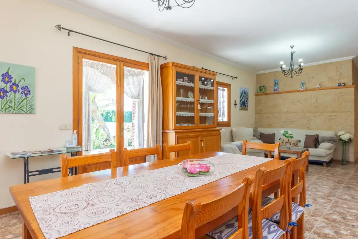 A dining area with a long wooden table and a seating area by the windows.
