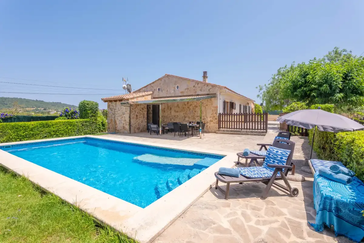 A swimming pool beside a stone house, with outdoor seating on the patio.